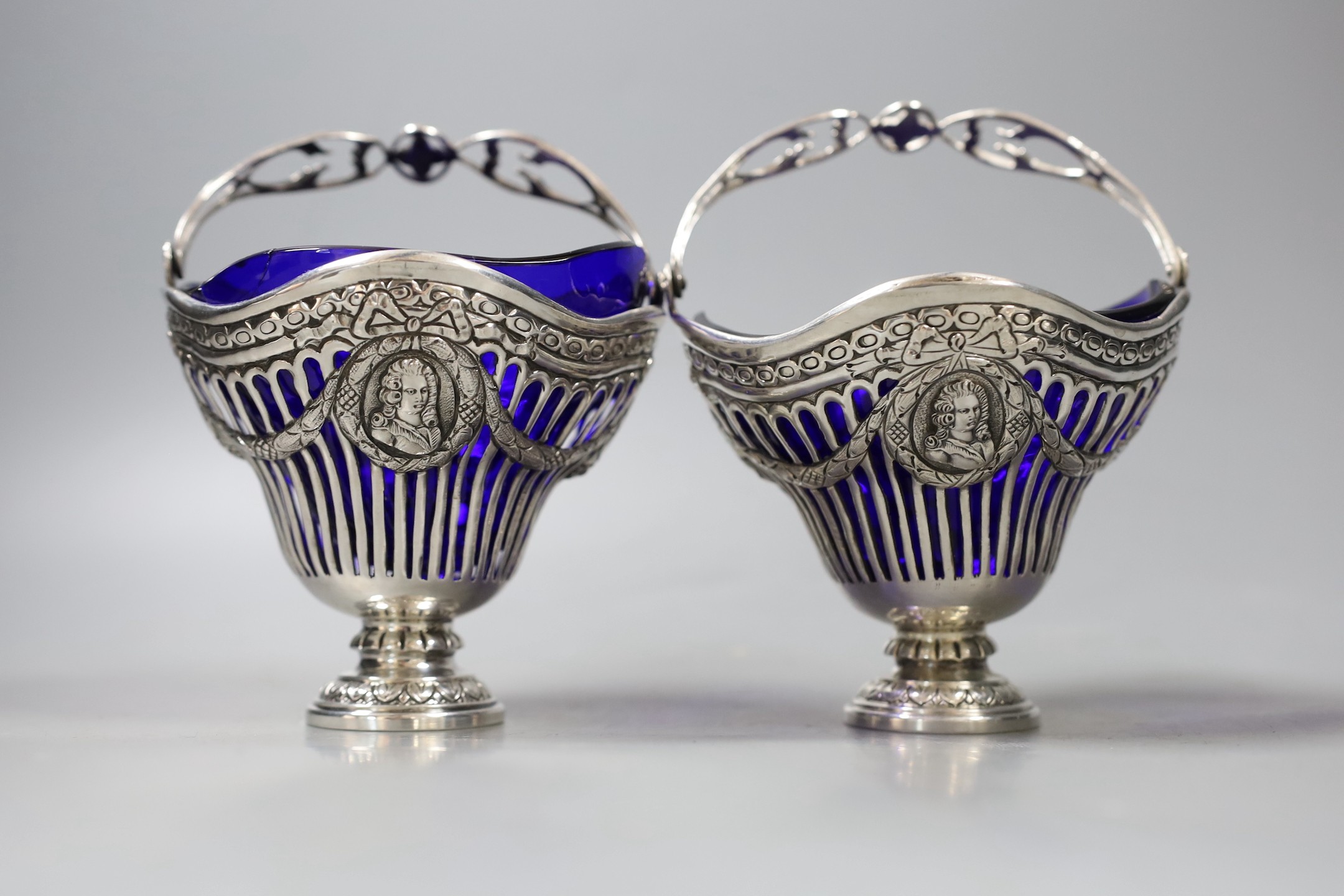 A pair of continental pierced white metal sugar baskets, with shaped blue glass liners, diameter 11.4cm.